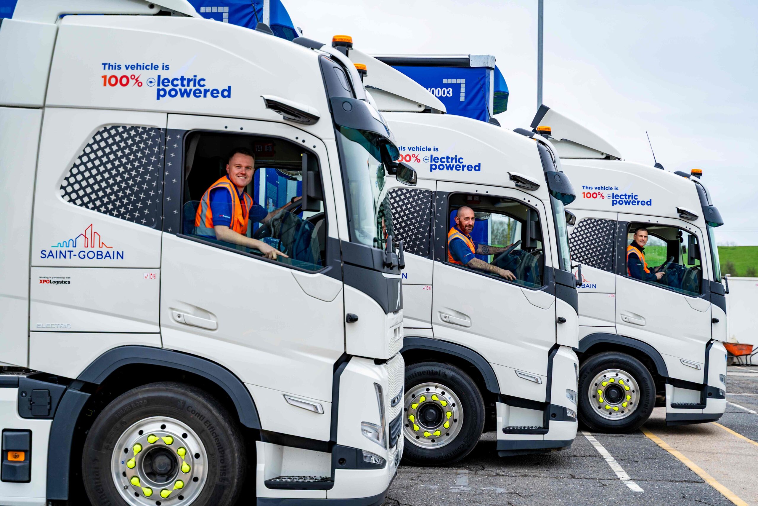 Three Saint-Gobain e-HGVs parked in a line with in orange high-vis sat in the driving seat