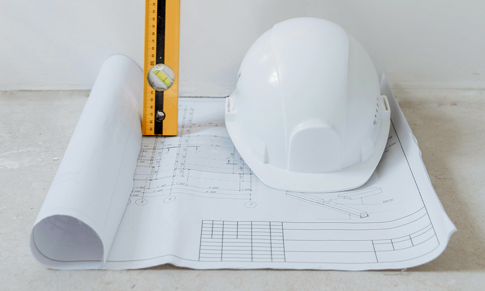 White hard workman's hat, with measurement ruler on top of a piece of paper with measurements and sketches on a plastered floor