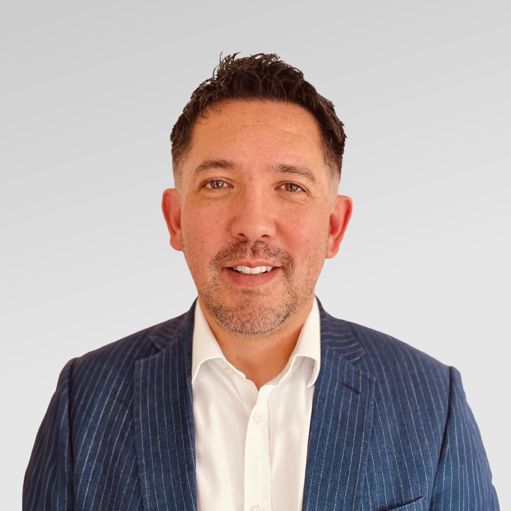 A photo of Ed Egerton, incoming Chief Legal & Commercial Officer, wearing a white shirt and a striped dark blue blazer with a plain off-white background