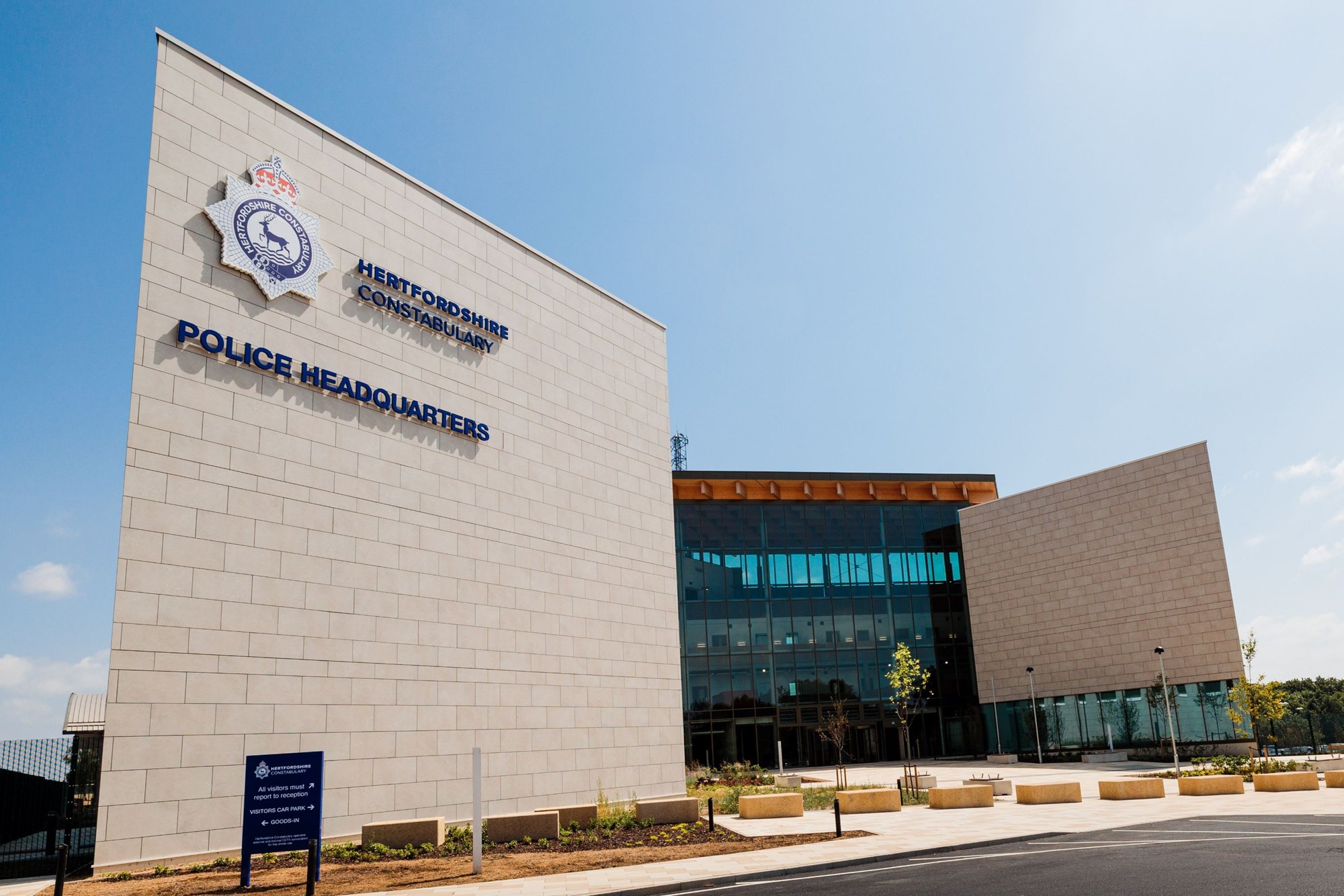 A long-shot of a beige brick building, separated by glass windows, set back against a pavement (the Hertfordshire Police Headquarters)