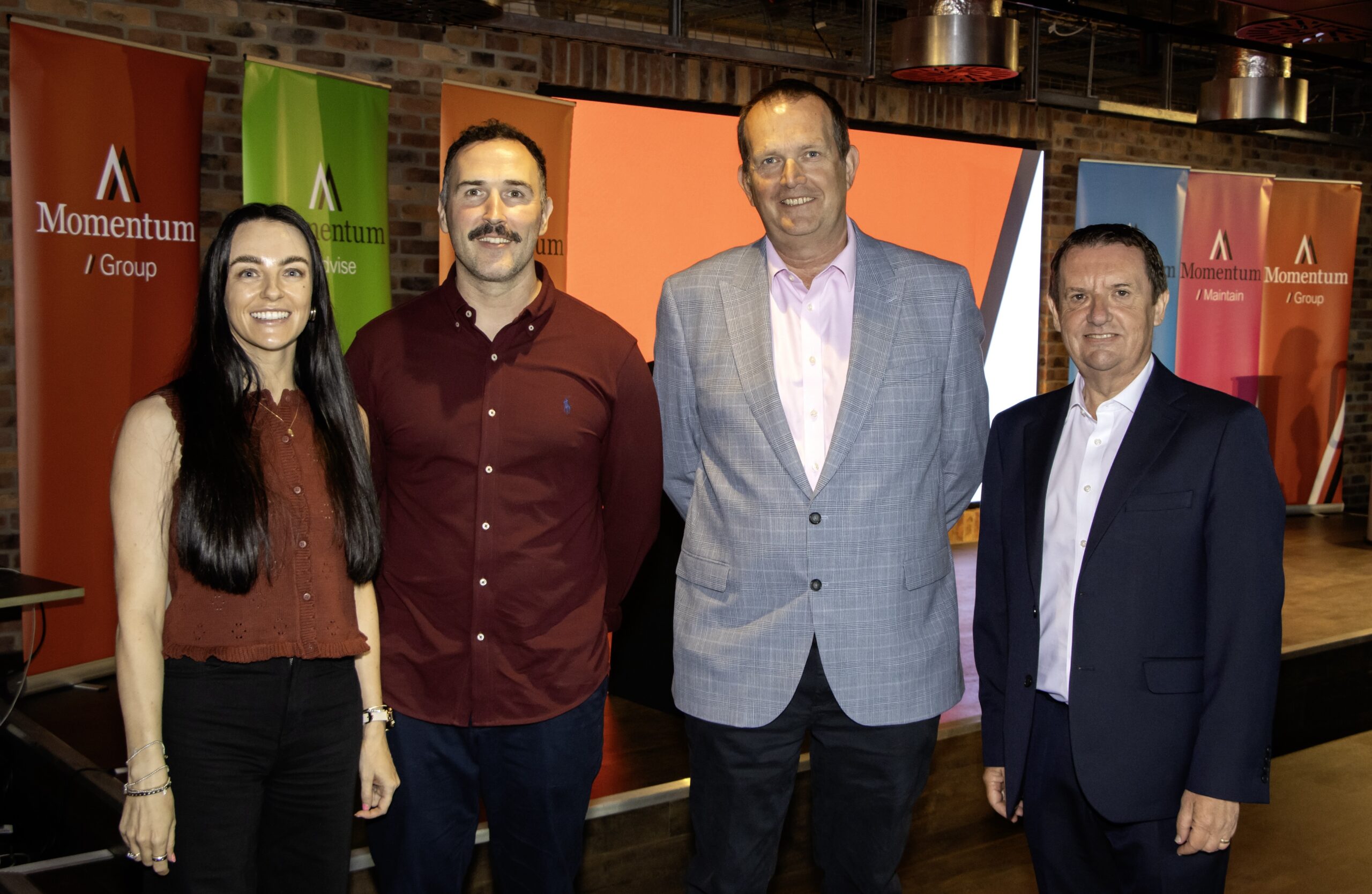 The members of Momentum Group x CPM Liverpool stood in front of 6 pop up multi-coloured branded banners at a presentation