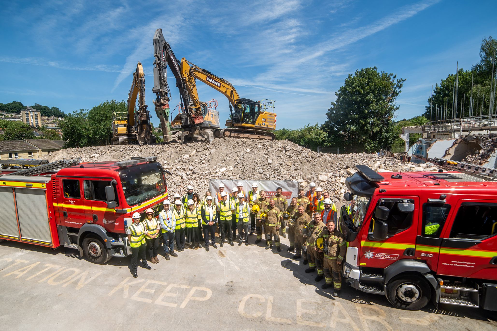 The team of Avon fire and rescue stood between two parked fire engines, with a large yellow digger in the background amongst dug up land