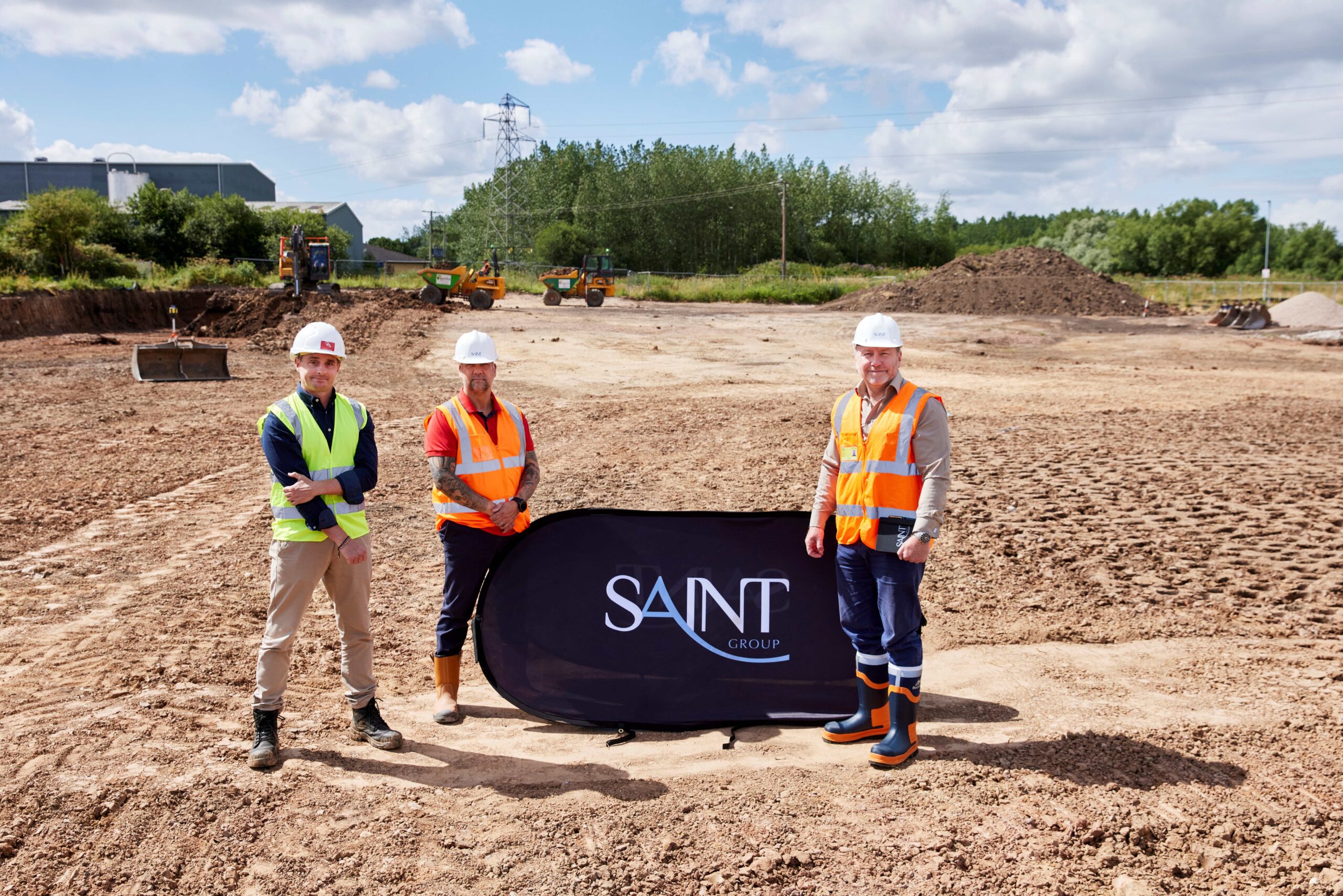 home-staging_01 Three workmen stood next to a pop up 'Saint Group' stand wearing his vis vests on a clear patch of land with two orange tractors and a digger in the background