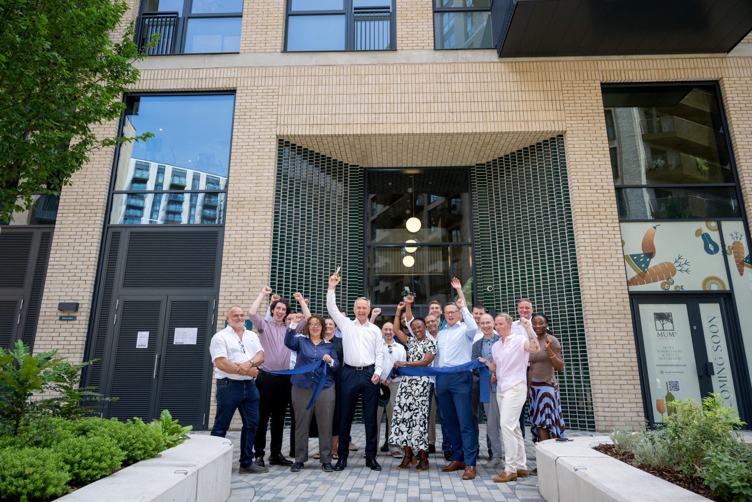 A group of people consisting of members of the Hill Group and L&Q stood outside a new build of apartments with their hands in the air, smiling and celebrating their success