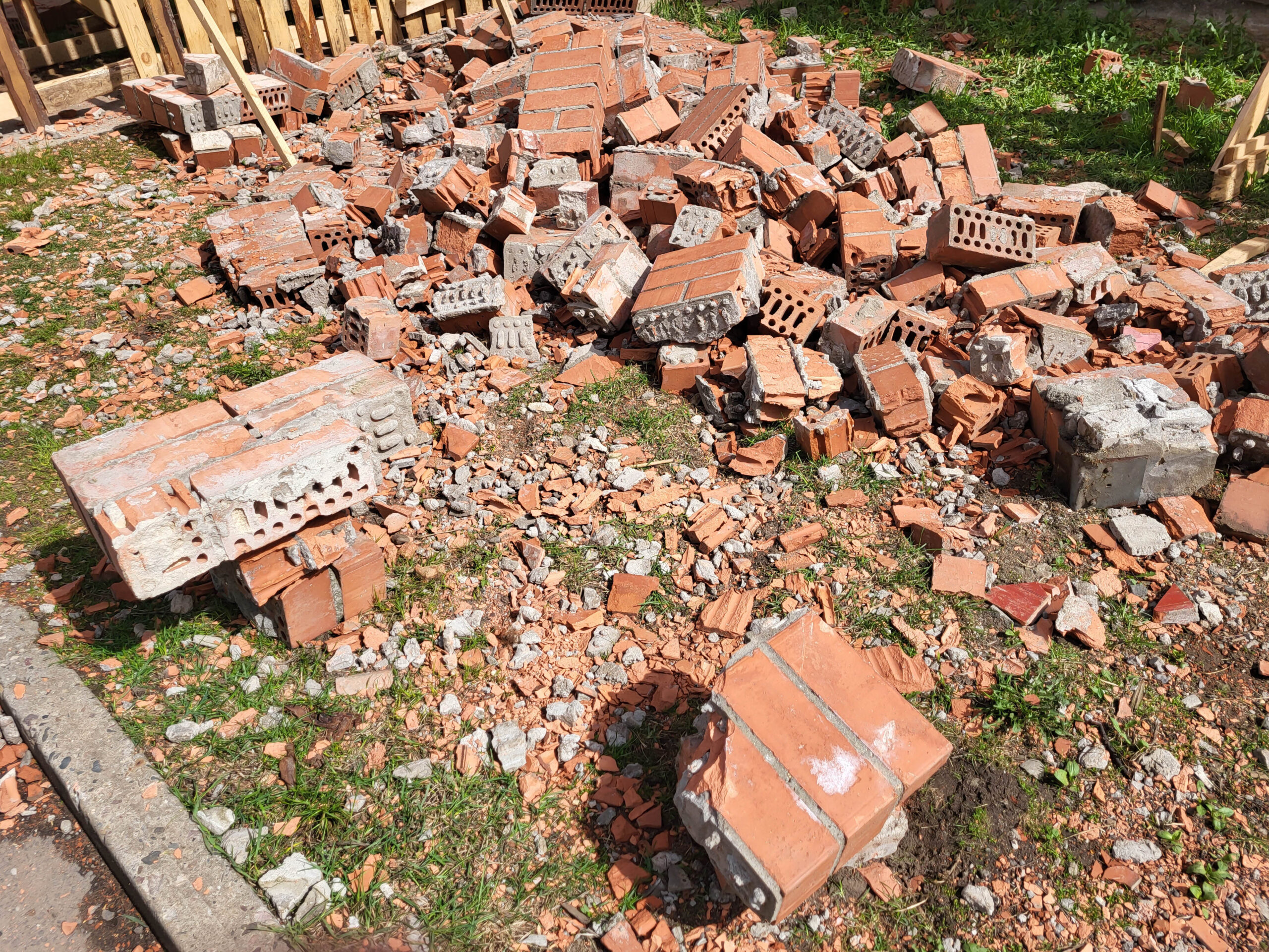A pile of broken red bricks lying on the grass repairing the wall of a house