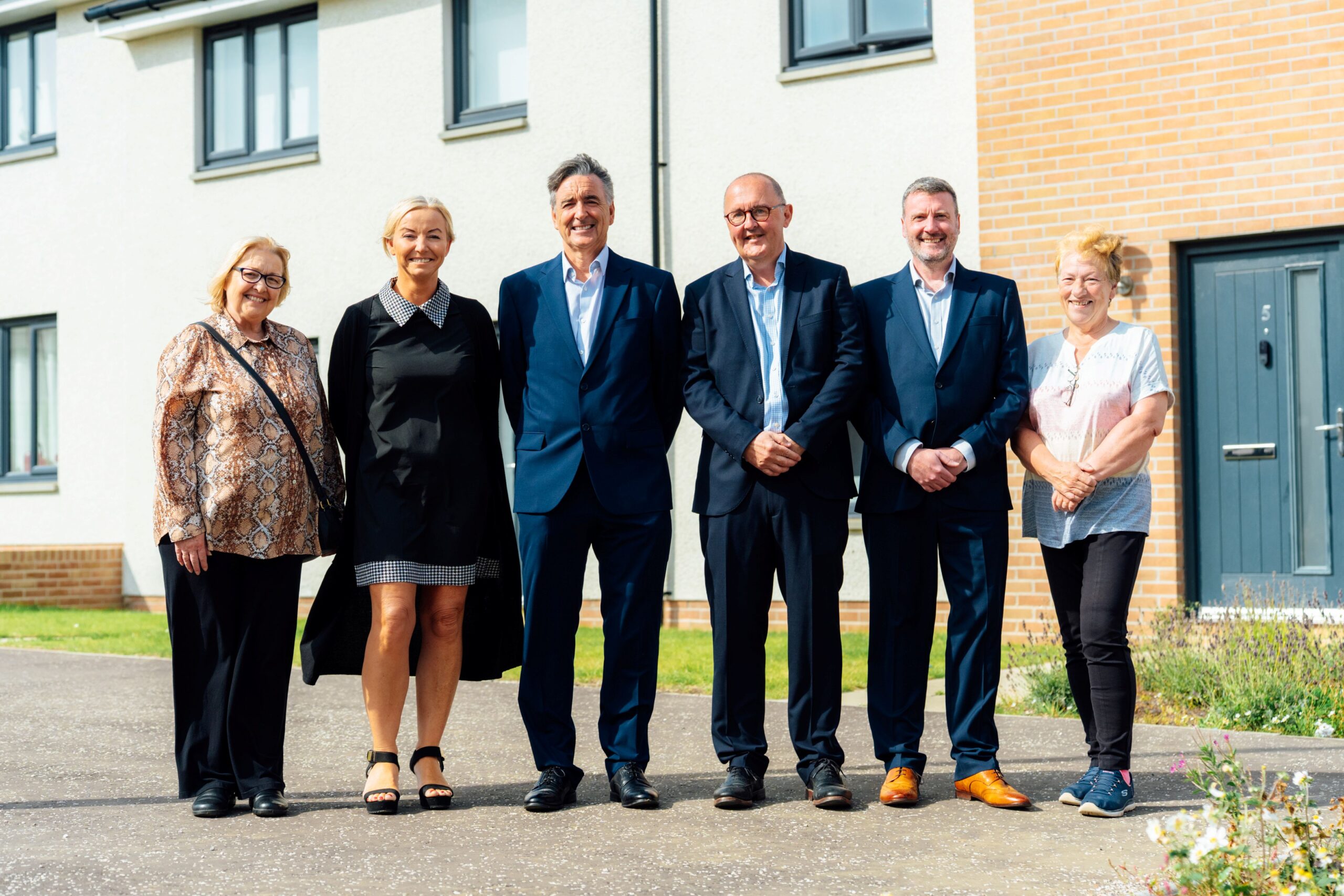 Six people stand together outside a modern housing development.