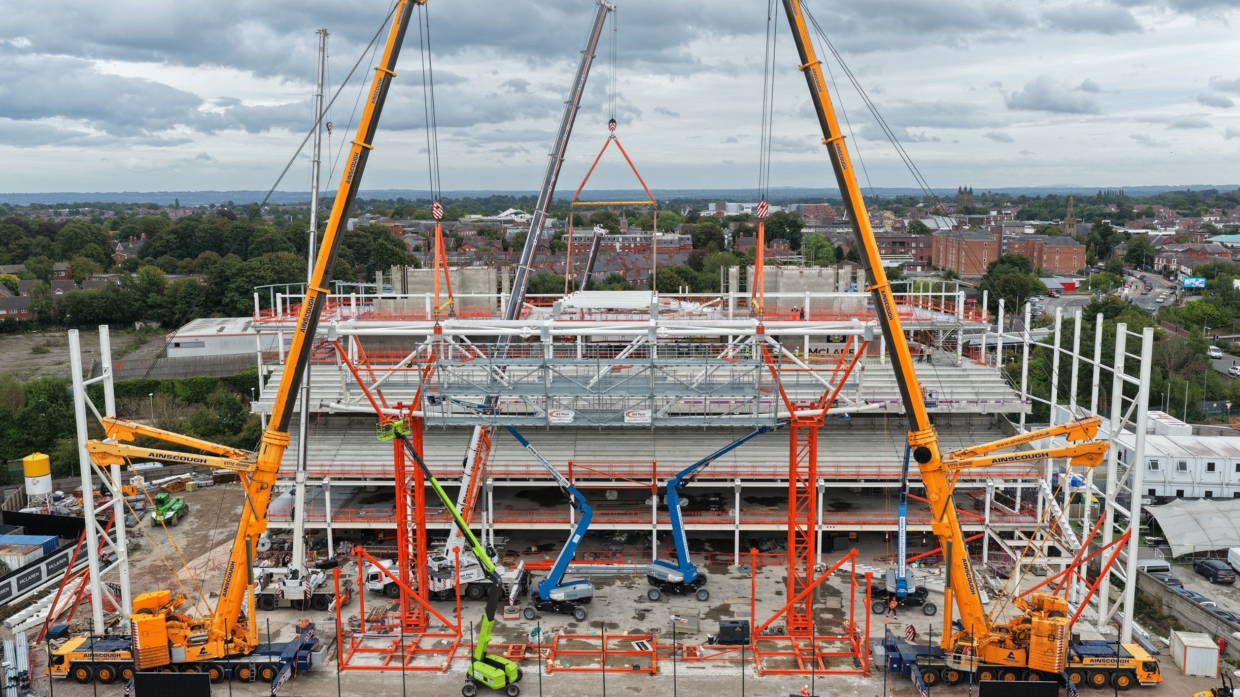 A birds eye view of the construction site of the Wrexham AFC Kop Stand which is being built, showing multiple diggers and vehicles and the surrounding industrial area