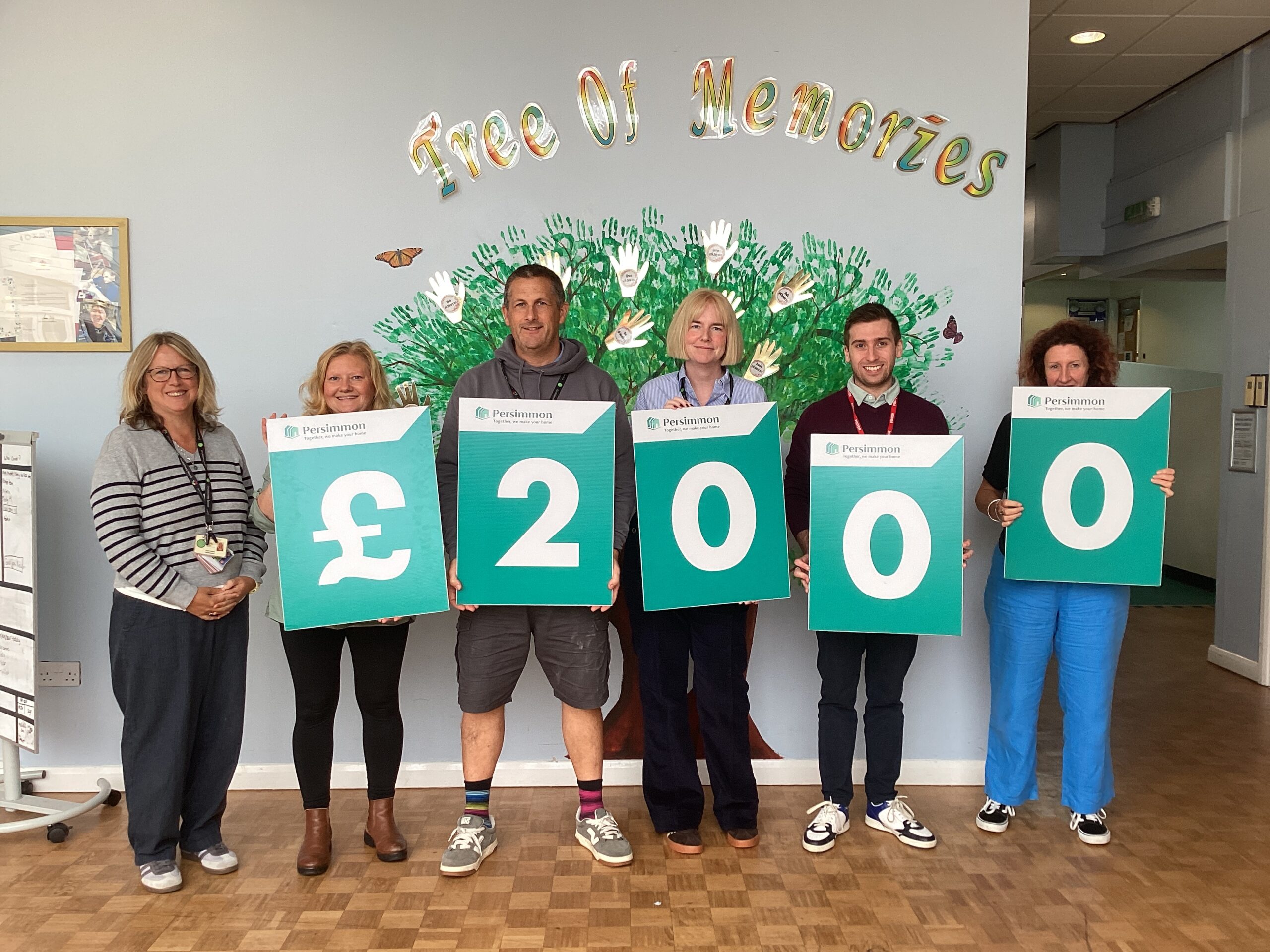 Six teachers stood in the school reception area holding individual Persimmon-branded card that reads 2,000 pounds