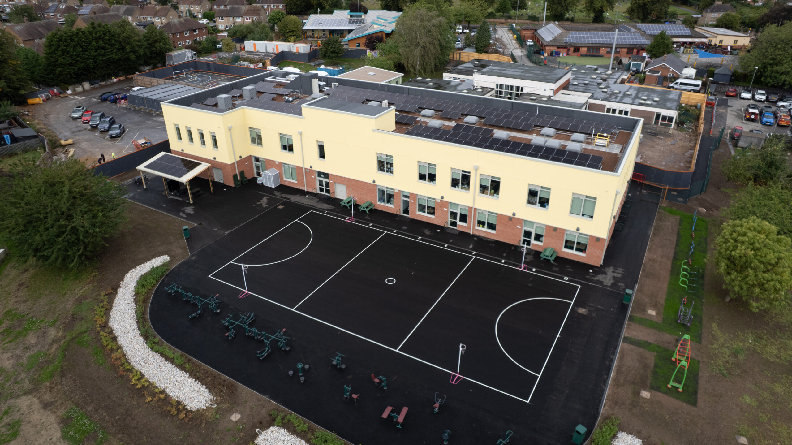 birds-eye-view of a school building and playground surrounded by houses and a car park